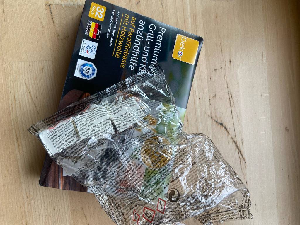 Auf einer Packung Grill- und Kaminzündhilfe liegen in Zellophan verpackte, getestete Anzünder.