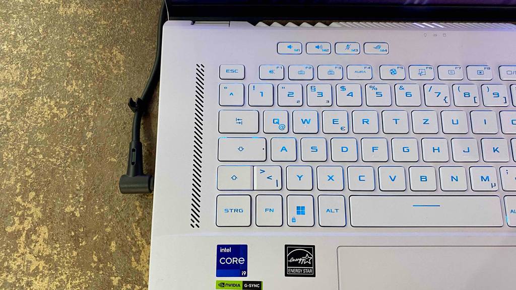 Detailaufnahme der beleuchteten Tastatur eines silberfarbenen getesteten Gaming-Laptops auf einem braunen Ausstellungstisch.