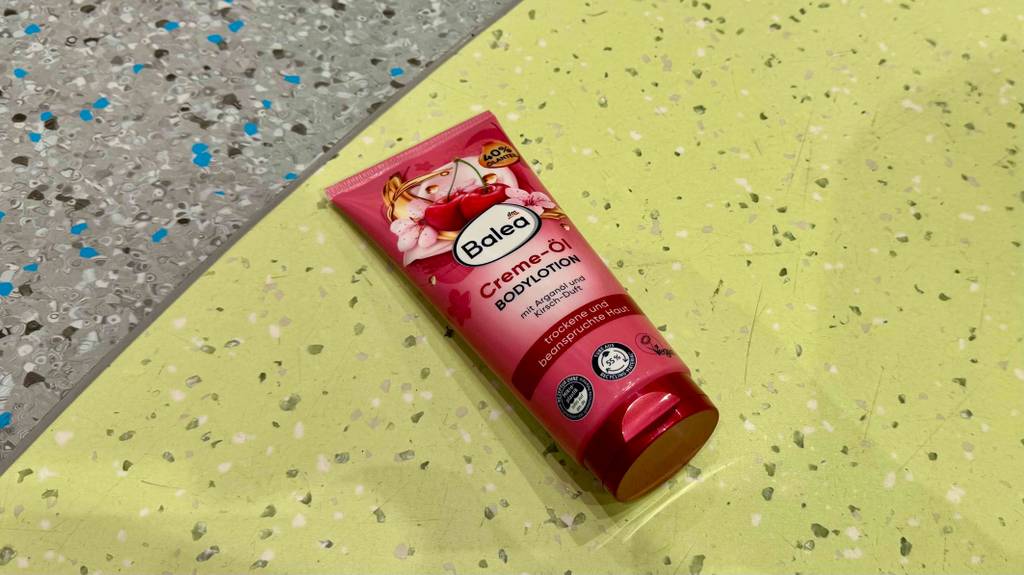 Im Test: BALEA Bodylotion in der roten Tube liegt auf einem Linoleum-Boden.