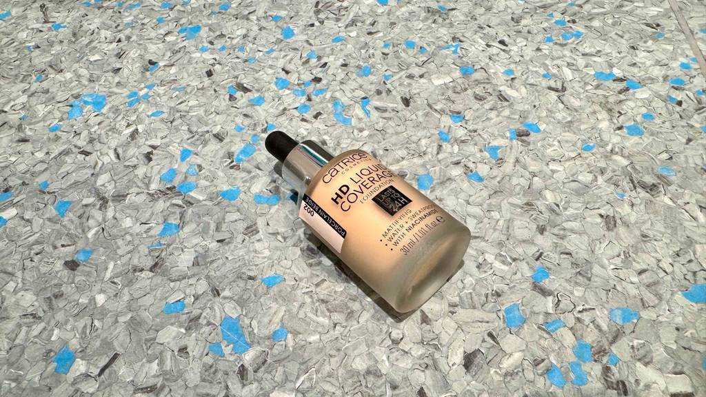 Catrice-Concealer im Test: Eine Flasche inklusive Pipette liegt auf einer Linoleumfläche.