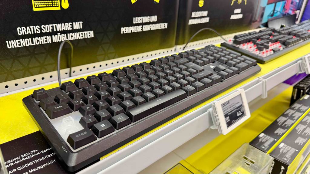 Getestet: Die Corsair-Tastatur inklusive Beleuchtung, steht vor weiteren Tastaturen auf einem gelben Ausstellungsregal.