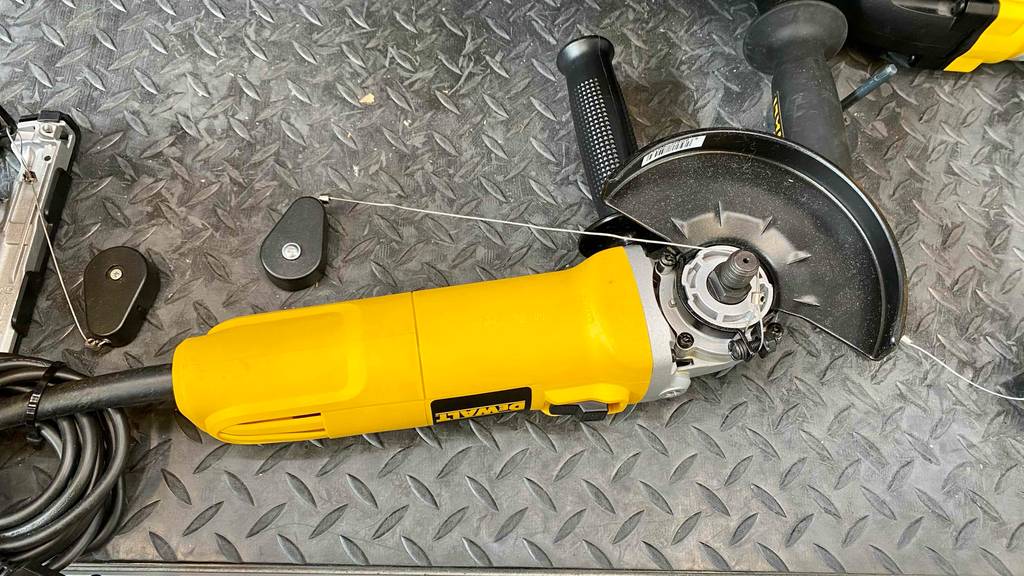 Ansicht der unteren Seite eines gelben DeWalt Winkelschleifers im Test, der gesichert auf einem grauen Metallregal im Verkaufsbereich liegt.