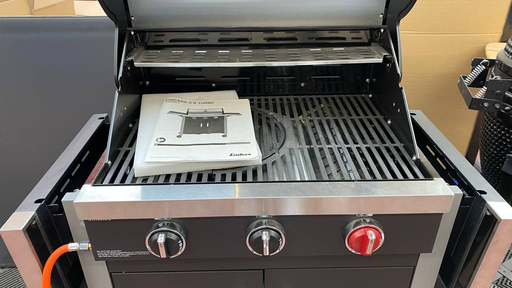 Enders-Gasgrill-Test: Vordere Ansicht des Gasgrills, mit Fokus auf die stufenlosen Regelschalter und den mehrstufigen Grillaufsatz inklusive Gebrauchsanleitung.
