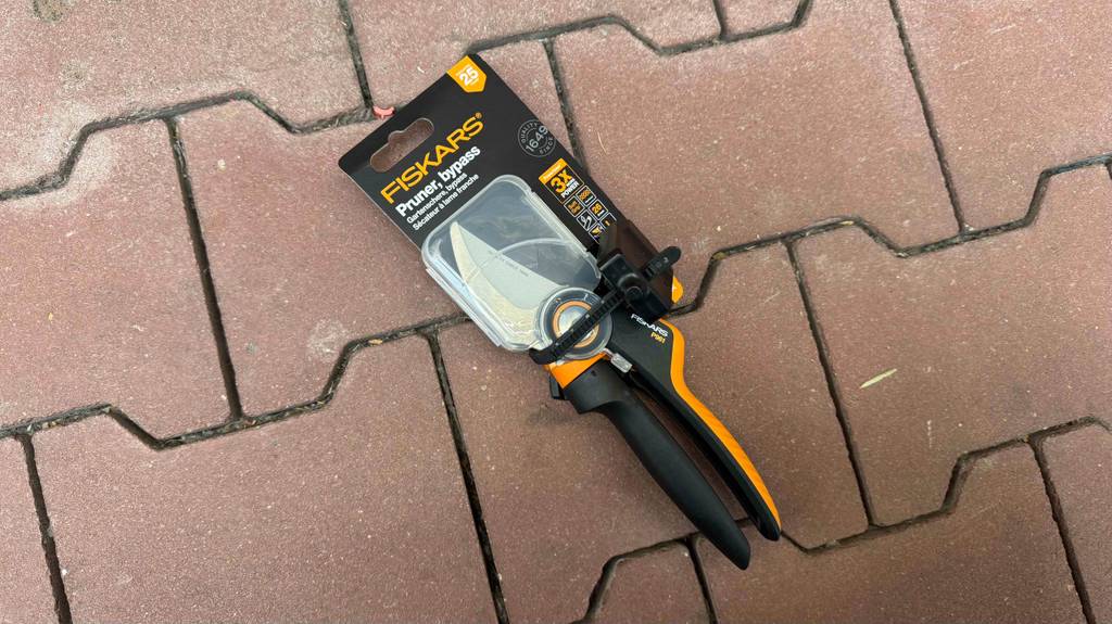 Eine Fiskars-Gartenschere im Test liegt originalverpackt auf einem roten Steinboden.