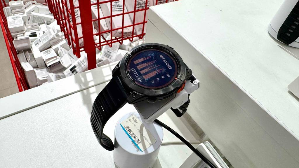 Eine schwarze getestete Garmin-Uhr liegt mit eingeschalteter Anzeige auf einem Ausstellungspodest im Verkauf.