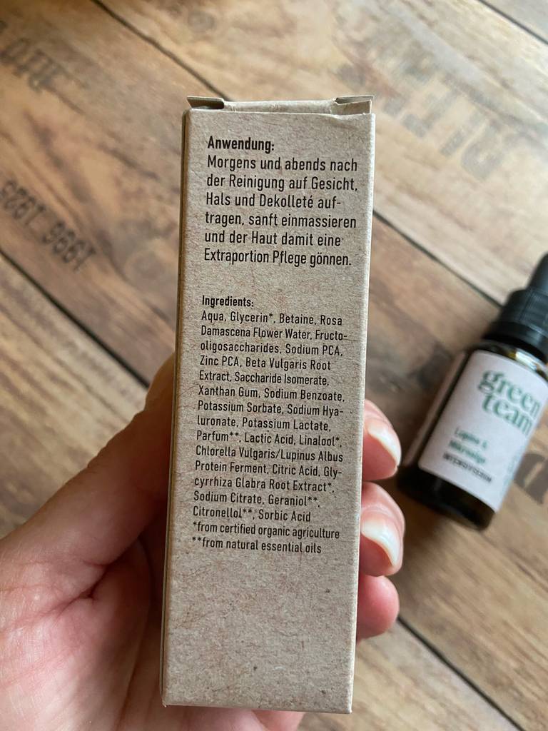 Eine Hand hält die Anwendungsbeschreibung sowie die Inhaltsstoffe, gedruckt auf der Verpackung der getesteten Glättungscreme, in die Kamera.