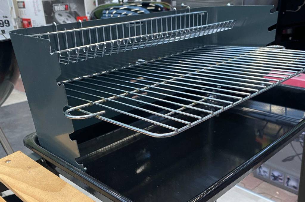 Nahaufnahme eines Grillwagens im Test: Metallrost und Holzablage im unteren sowie seitlichen Bereich seines Metall-Gestells.