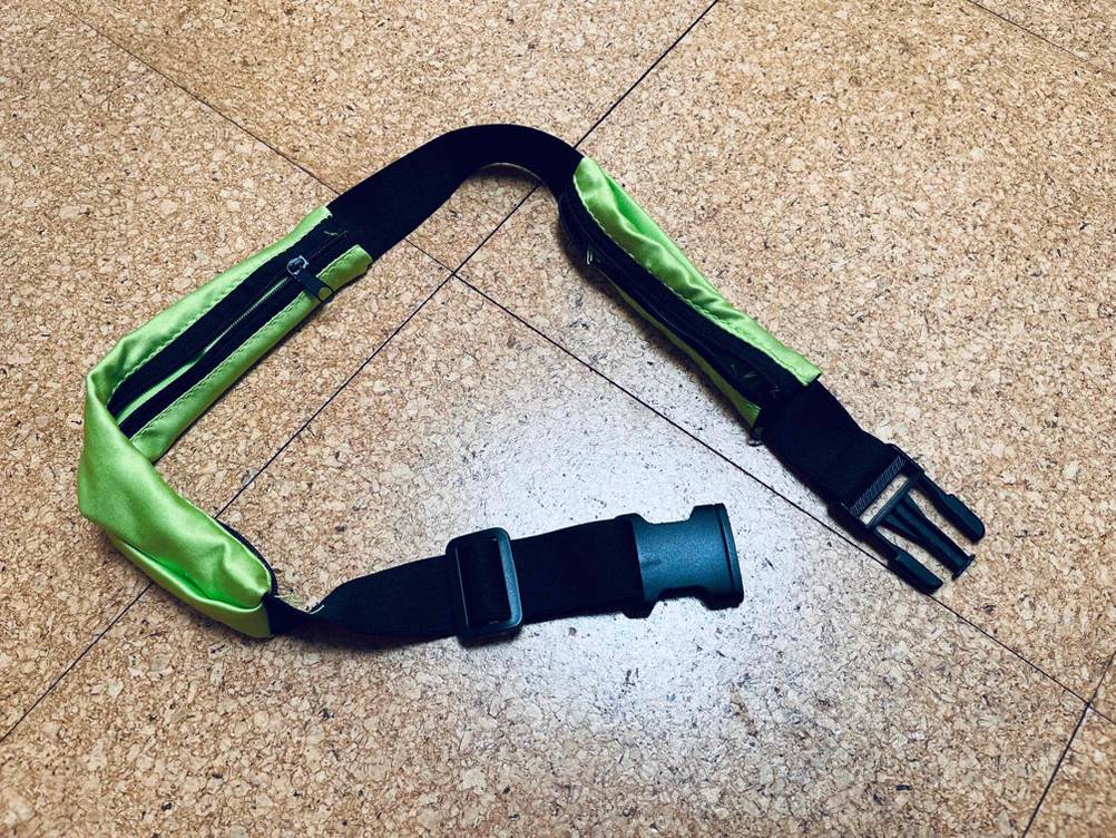 Schwarzer Laufgürtel im Test liegt in seiner gesamten Länge inklusive zweier grüner Taschen auf einem Fliesenboden.