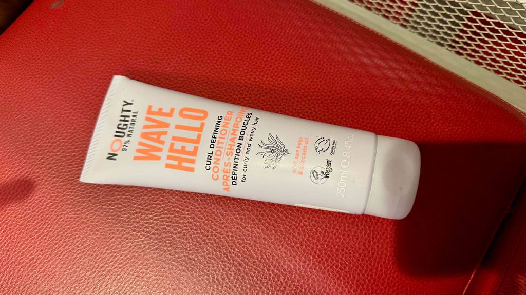 Getestet: Ein Locken-Conditioner in einer weißen Tube liegt auf einem roten Lederbezug.