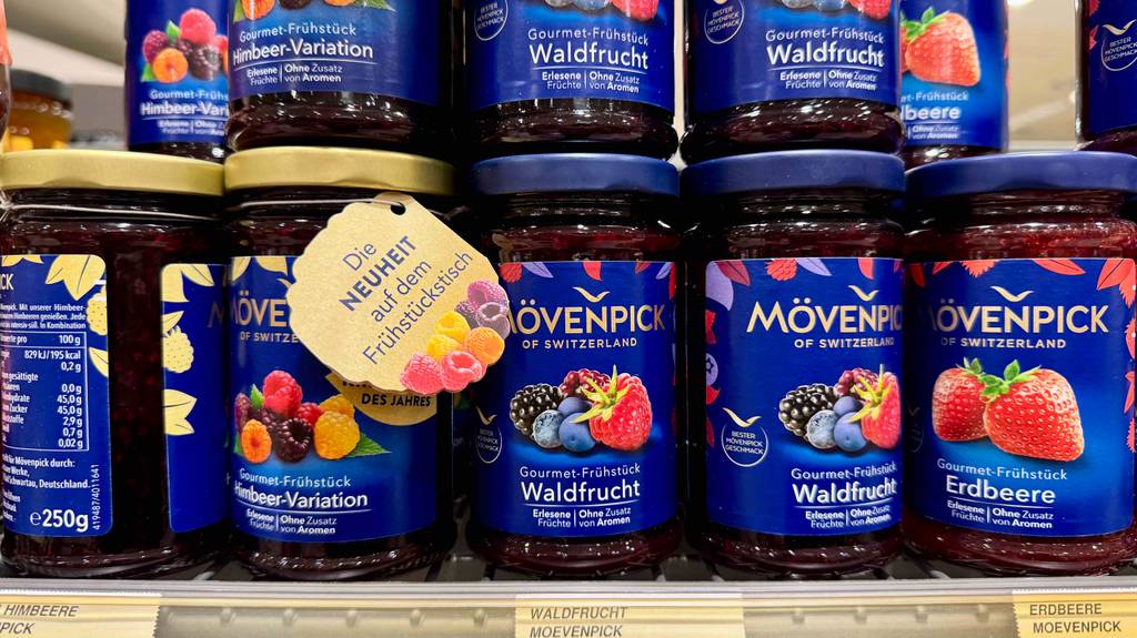 Mehrere Gläser Waldfrucht-Mövenpick-Marmelade stehen auf einem Verkaufsregal neben weiteren Fruchtsorten im Glas.