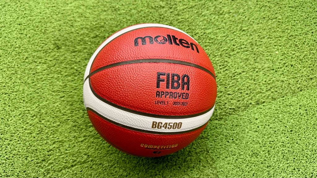 Basketbälle im Test: Ein rotes Modell BG4500 mit beigefarbenen Streifen, der Marke Molten, liegt auf einem grünen Kunstrasen.