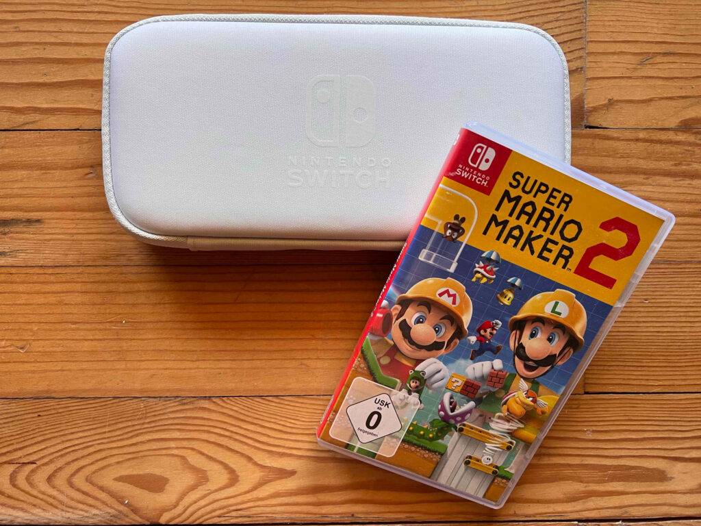 Im Test: ein Nintendo-Switch-Spiel Super Mario Maker 2 lehnt an einer weißen Nintendo-Switch-Controller-Tasche auf einer Holzfläche.
