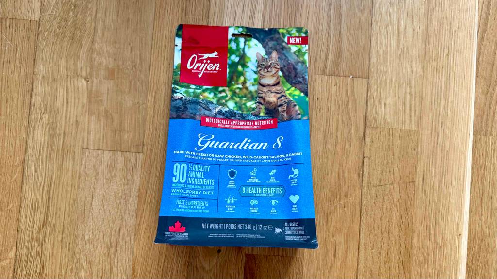 Das Katzen-Trockenfutter von Orijen im Test liegt innerhalb einer wiederverschließbaren 340-g-Frischhaltetüte auf einem Holzboden.