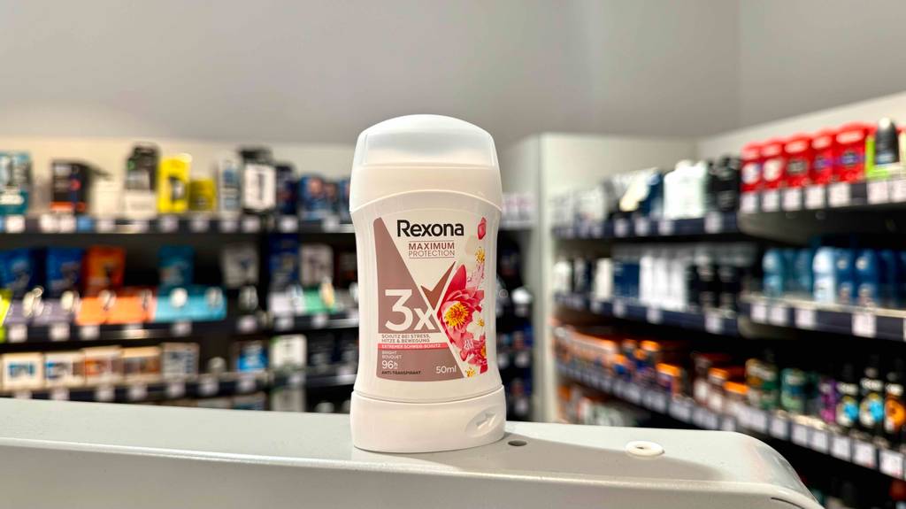In einem Drogeriemarkt befindet sich ein Stick Rexona-Deodorant im Test vor Verkaufsregalen.