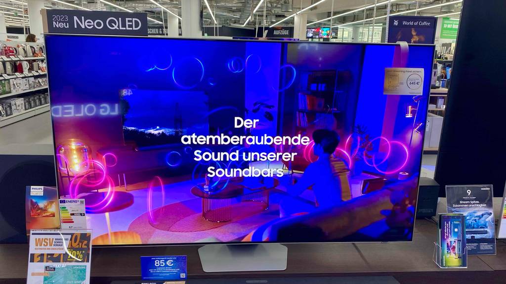 Ansicht von vorn auf den eingeschalteten Bildschirm eines Samsung-Fernsehers (65 Zoll) im Test, der in einem Verkaufsbereich steht.