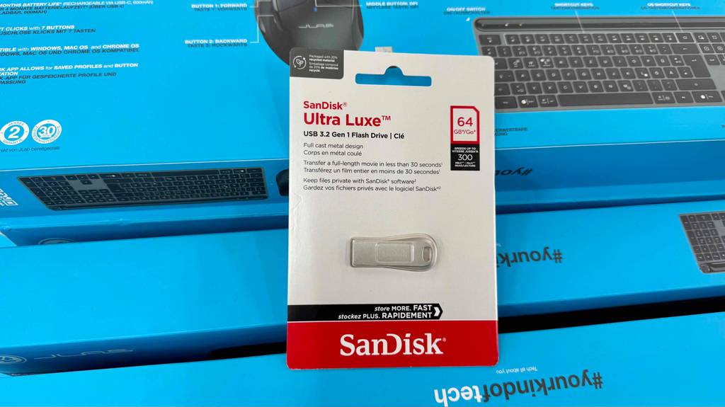 Getestet: ein SanDisk Ultra Luxe mit 64 GB Speicherplatz innerhalb der Verpackung auf mehreren Kartons mit Tastaturen.