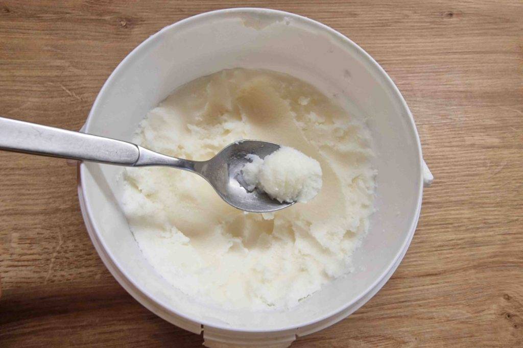 Getestete Sheabutter in einem weißen Behältnis, darüber ein Teelöffel mit Sheabutter.