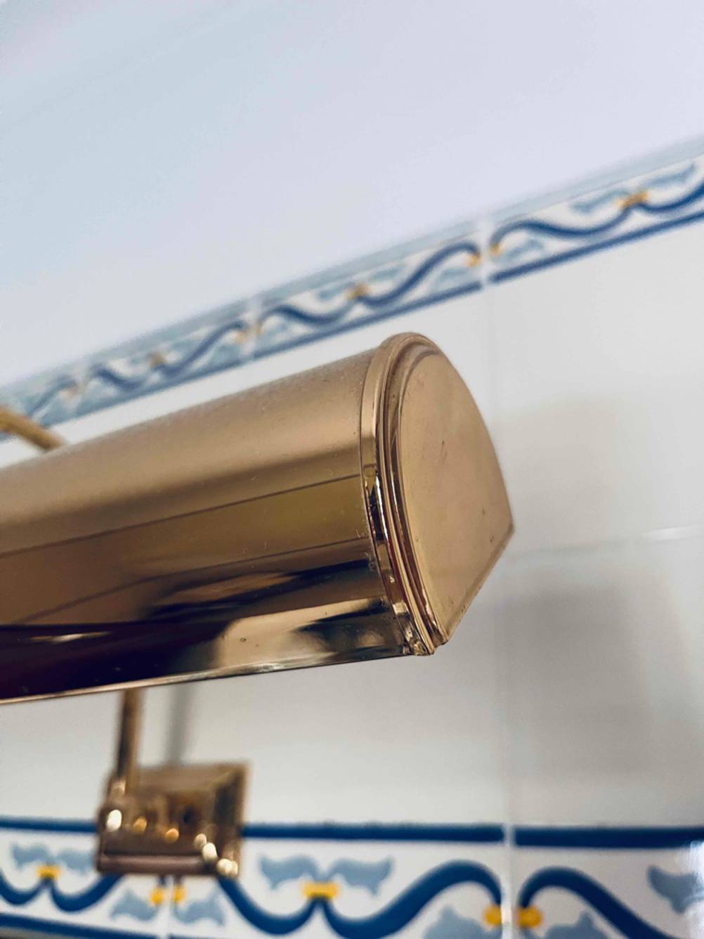 Spiegelleuchte-Test: Detailaufnahme des goldenen Materials vor einer Fliesenwand.