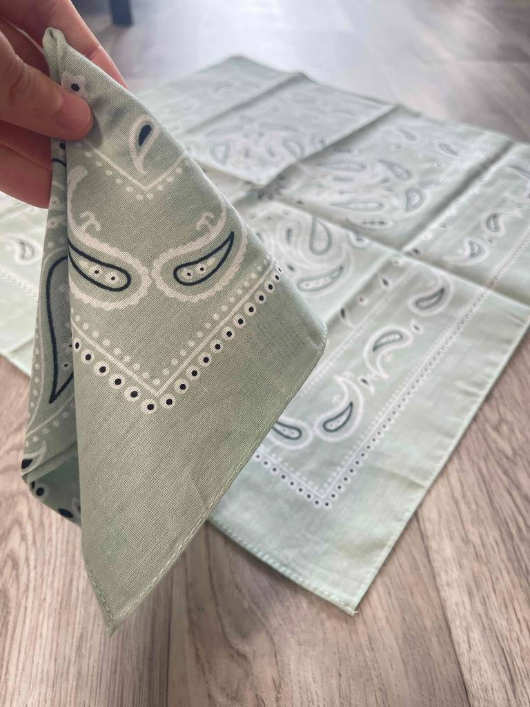 Bandana-Test: Eine Hand hält ein graues Kopftuch vor einem weiteren Kopftuch, das auf dem Tisch liegt.