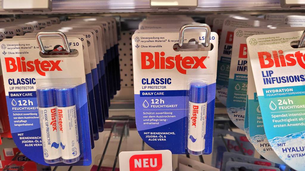 Mehrere Produktverpackungen mit getesteter Blistex-Lippenpflege befinden sich an einem Verkaufsregal.