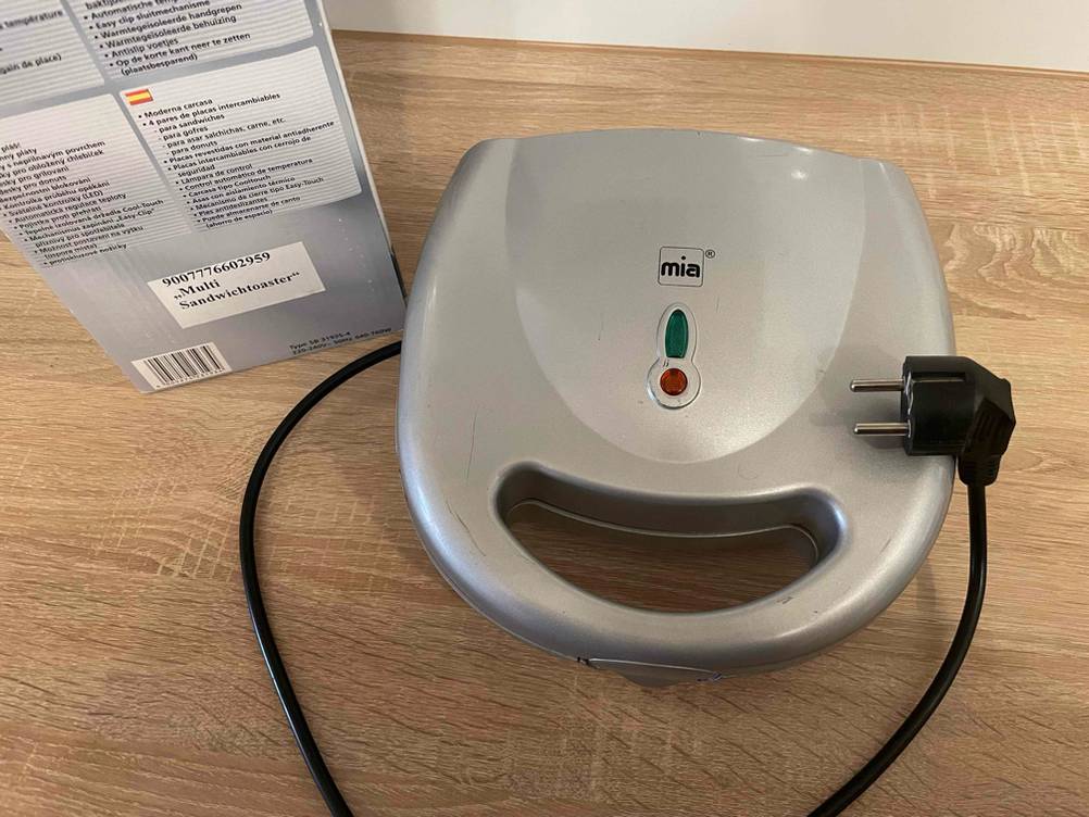Ansicht von oben auf einen Sandwichmaker 3 in 1 im Test, der inklusive Kabel neben seiner Verpackung auf einem Tisch steht.