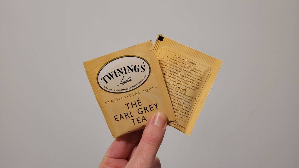 Eine Hand hält zwei versiegelte Teebeutel mit Twinings-Tea im Test vor einer weißen Wand.