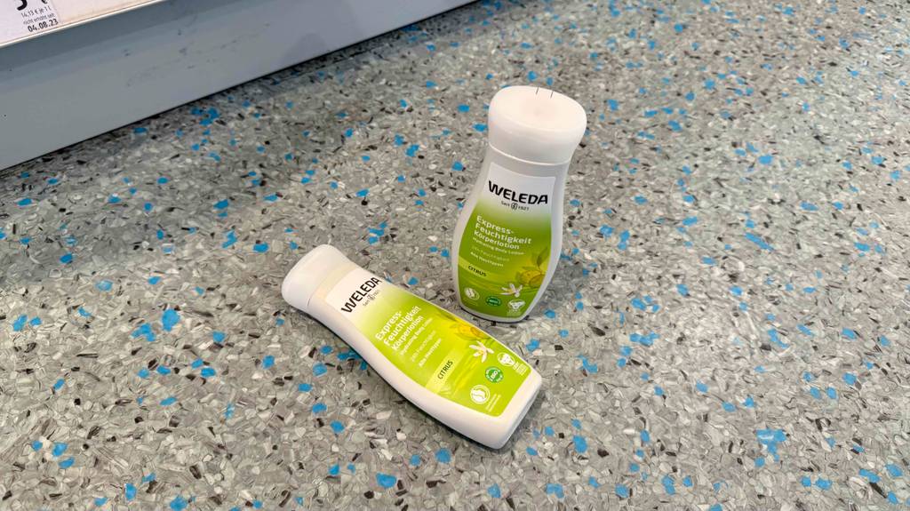Zwei Kunststoffflaschen mit WELEDA-Bodylotion im Test befinden sich auf einem Linoleumboden.