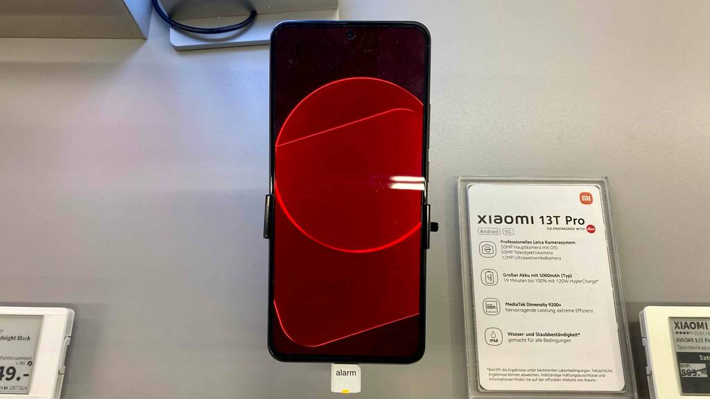 Xiaomi-Handy im Test: ein eingeschaltetes Modell 13T Pro, mit rotem Display, neben seiner Kurzbeschreibung auf einem Ausstellungs-Ständer.