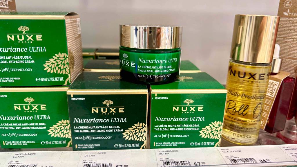 Nuxe-Gesichtscremes im Test: Mehrere grüne Verpackungen mit 50-ml-Tiegel befinden sich auf einem Verkaufsregal für Nuxe-Produkte.