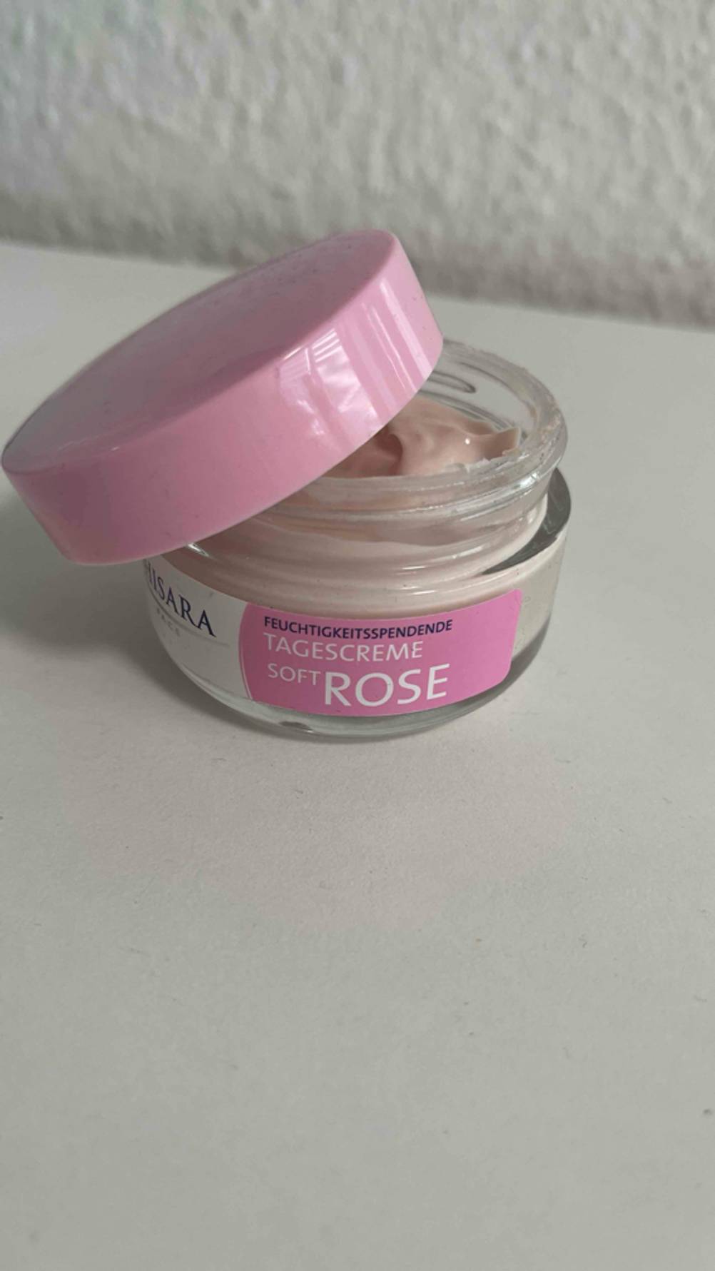 Die getestete Rosencreme befindet sich in einem geöffneten Tiegel mit rosafarbenem Deckel, der auf einer weißen Oberfläche steht.