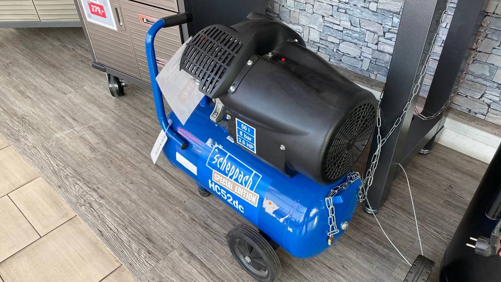 Blauer, getesteter50-Liter-Kompressor von Scheppach steht angekettet in einem Verkaufsraum.