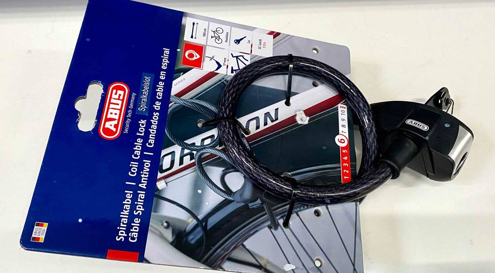ABUS-Fahrradschloss-Test: schwarzes Abus Spiralkabel, mit Fokus auf die Schließeinheit, auf seiner blauen Verkaufspappe auf weißer Fläche.