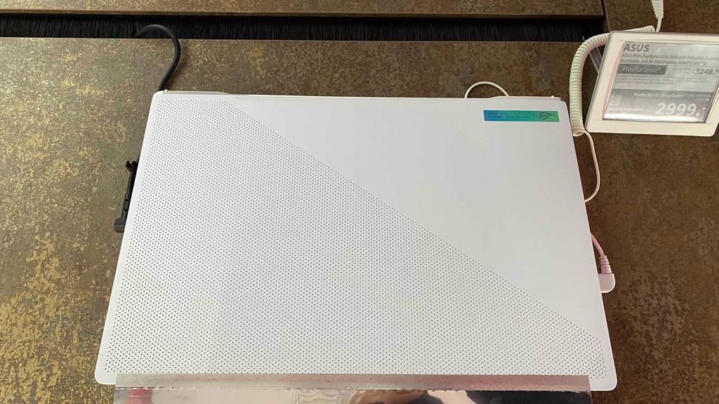 Ansicht von oben auf einen zugeklappten silberfarbenen Asus-Gaming-Laptop, mit Fokus auf die Belüftungslöcher des Bildschirms und das Preisschild daneben.