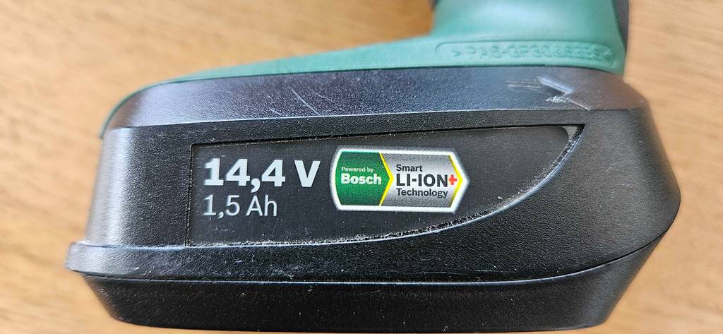 Detailansicht des an einem grünen getesteten Bosch-Akkuschrauber montierten Akkus inklusive 14,4 Volt „LI-ION+“ Technologie.