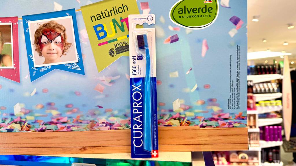 Getestet: Eine Curaprox-Zahnbürste in der Verpackung befindet sich vor einem Plakat im Drogeriemarkt.