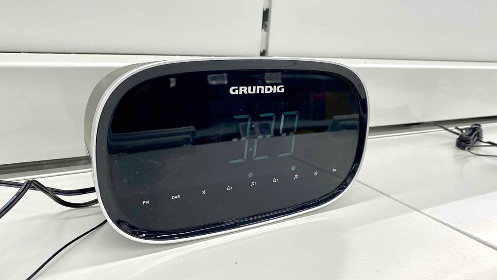 Ein eingeschalteter DAB-Radiowecker im Test steht auf einem weißen Verkaufsregal.