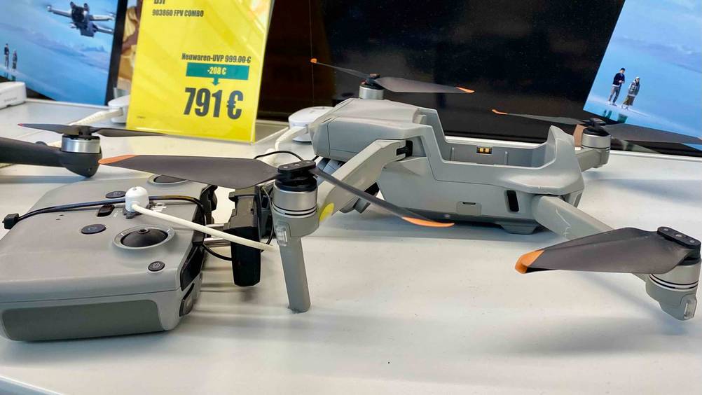 Im Test: Eine DJI-Drohne in Hellgrau befindet sich inklusive Steuerelement auf einer weißen Verkaufsfläche inklusive gelbem Preisschild.