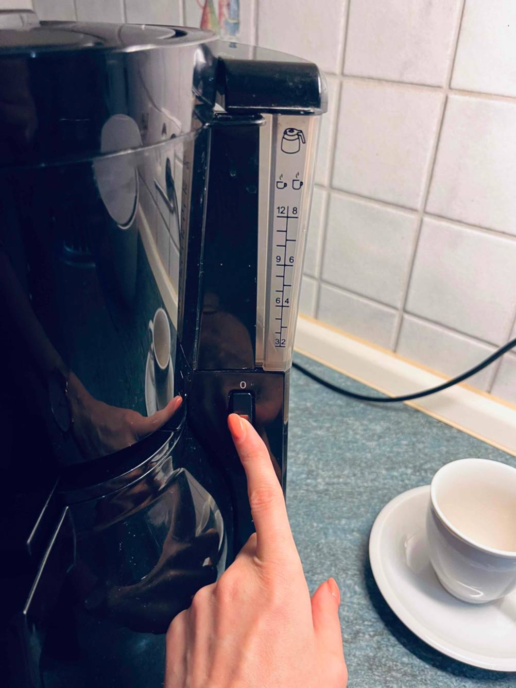 Zeigefinger berührt Einschaltknopf an einer schwarzen, getesteten Kaffeemaschine mit Direktbrühsystem.