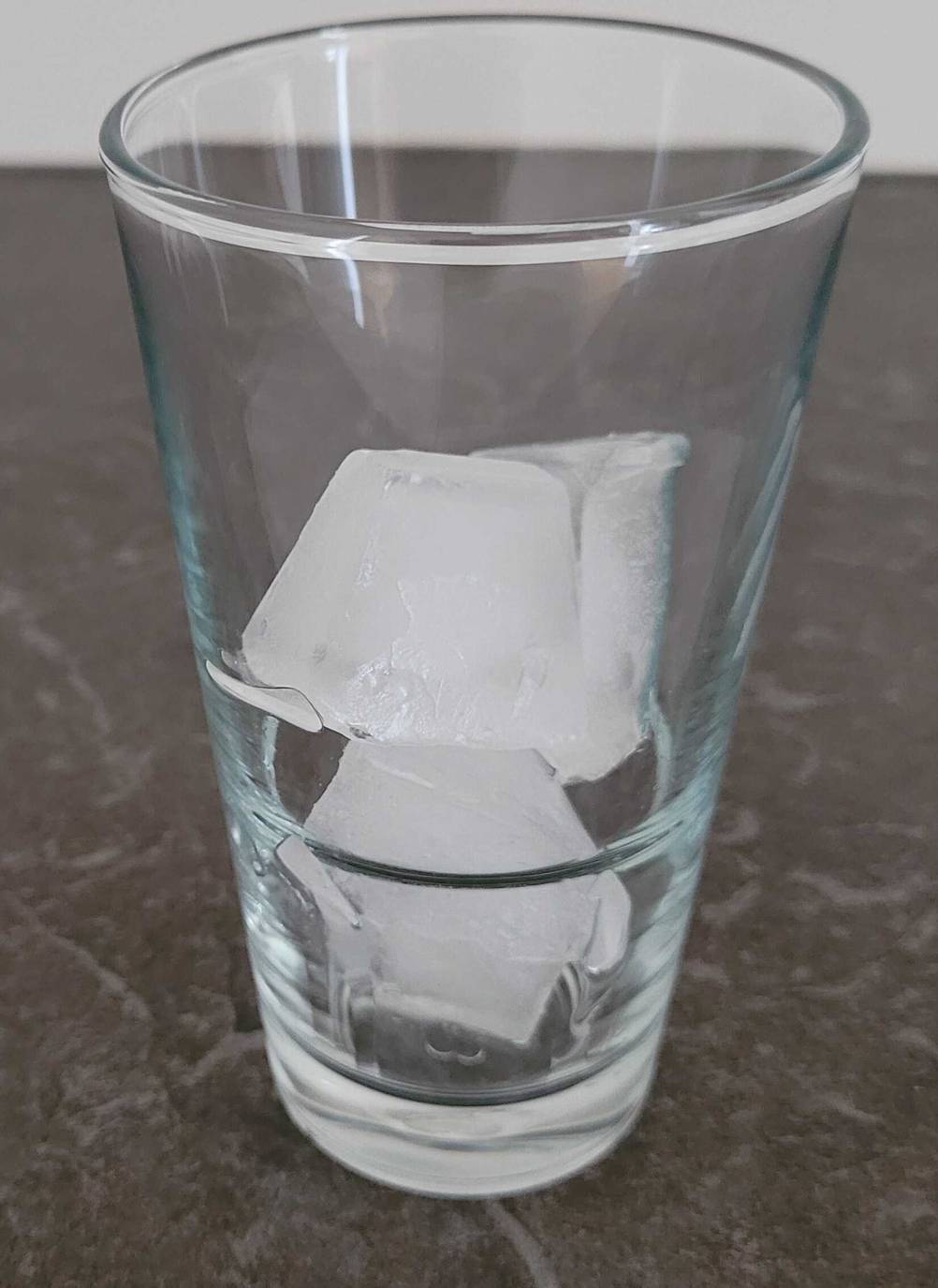 Eiswürfelformen im Test: Ein Glas mit eckigen Eiswürfeln steht auf einer anthrazitfarbenen Oberfläche.