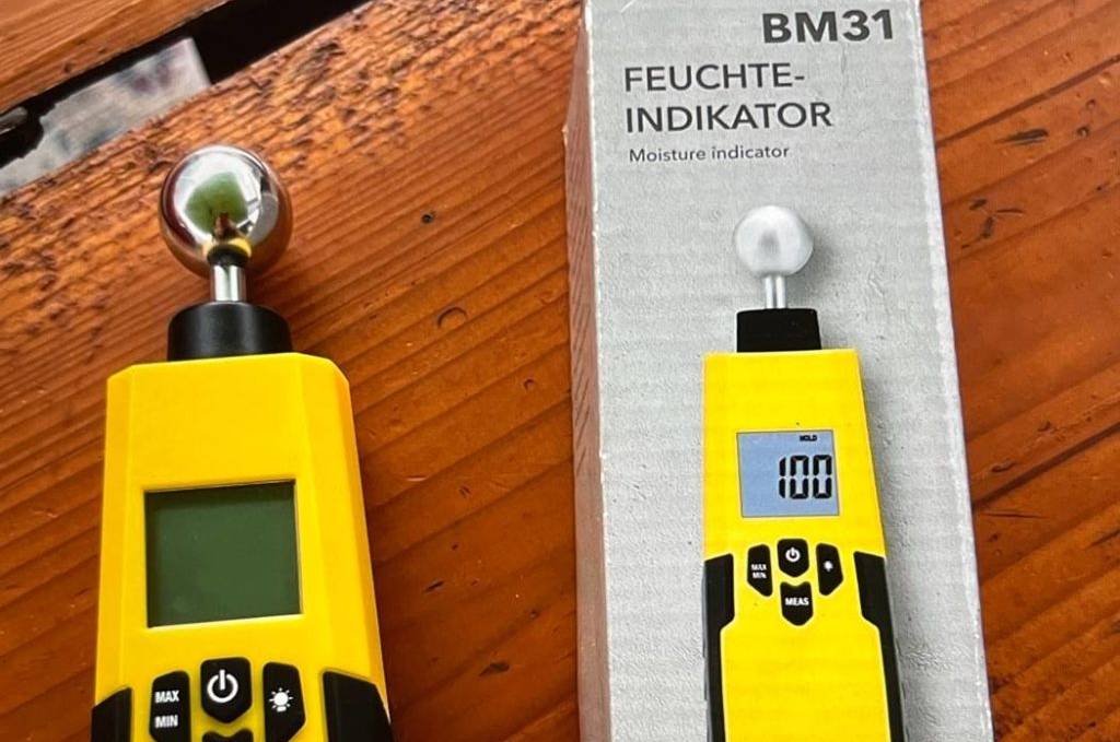 Feuchtigkeitsmessgerät im Test: gelber Trotec BM31 Feuchte-Indikator liegt ausgepackt neben der Verpackung auf Holzuntergrund.