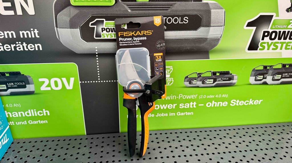 fiskars-gartenschere im test: die noch verpackte Gartenschere lehnt an einer Packung mit Akkus der Marke.