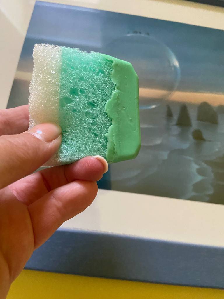 Eine Hand hält die grüne, getestete Gesichtsseife inklusive Schwamm über einem Waschbecken.