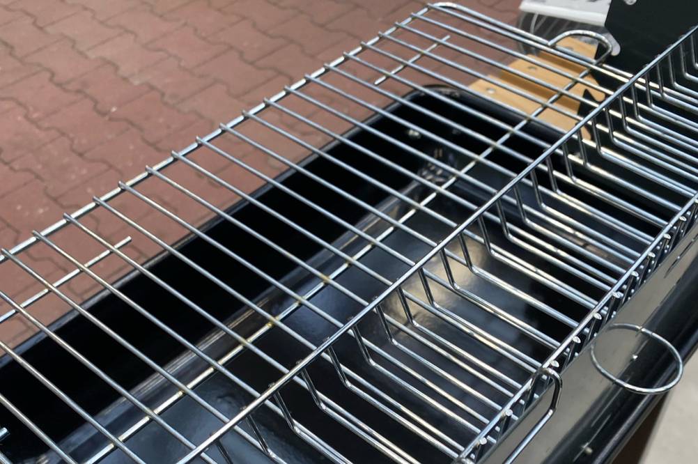 Detailansicht von schräg oben eines getesteten Grillwagens inklusive Metallrost und Holzablage im unteren Bereich seines Gestells.