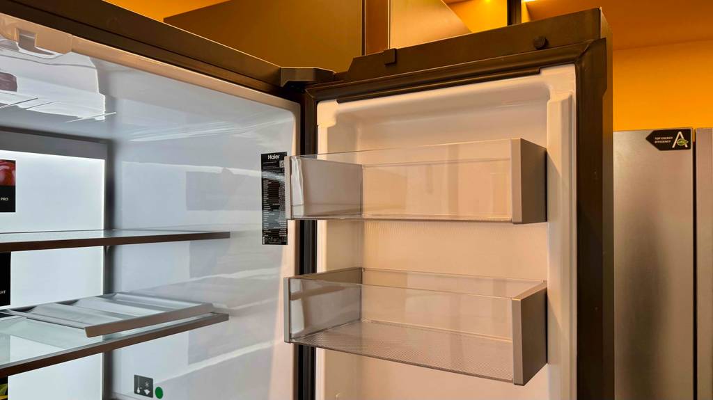 Haier-Side-by-Side-Test: Der zweitürige Kühlschrank steht geöffnet mit Blick auf die oberen Ablageflächen aus Glas in einem Ausstellungsbereich.