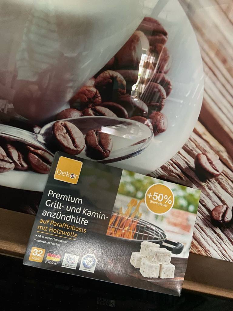 Anzünder-Test: Eine Packung Grill- und Kaminzündhilfe liegt auf einem Frühstücksset mit Kaffeebohnendruck.