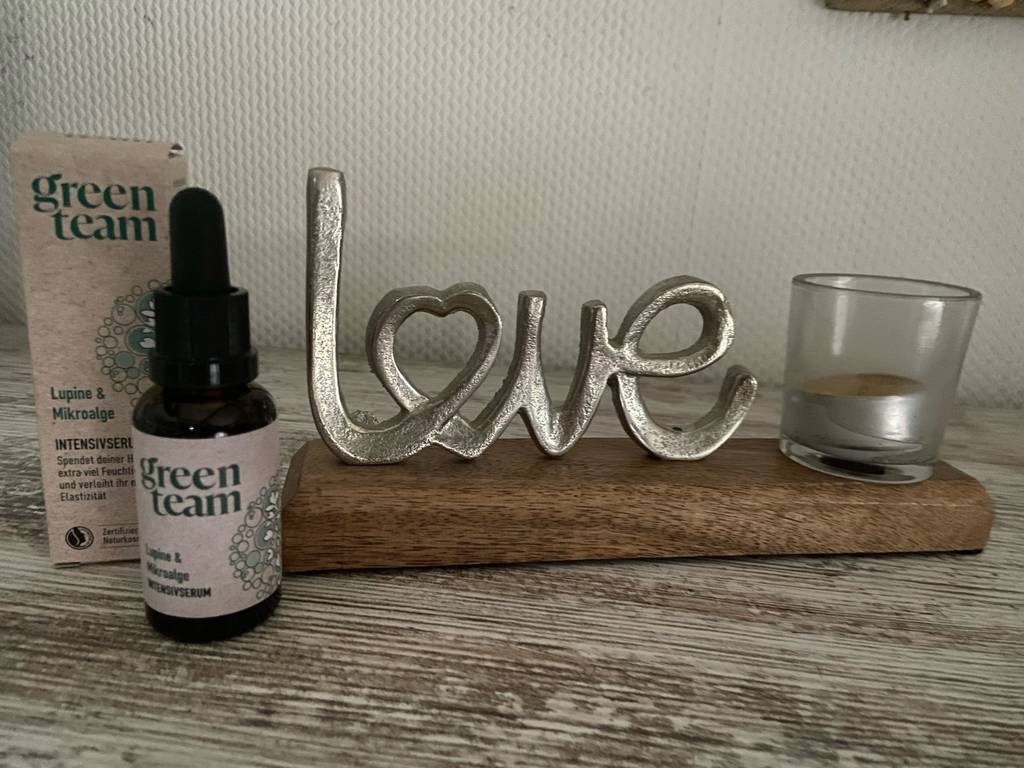 Im Test: Die Glättungscreme befindet sich in einer braunen Flasche mit Pipette, die neben ihrer Packung vor einer Tischdekoration steht.