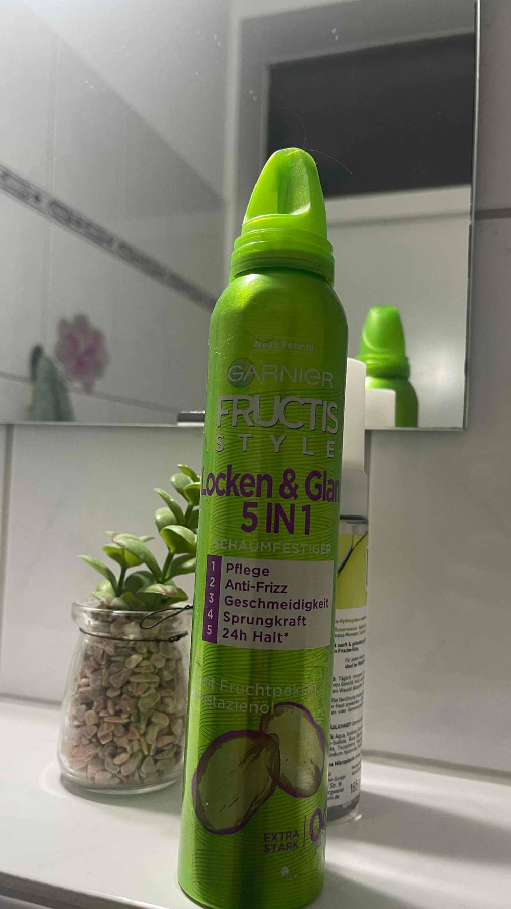 Vor einem Badezimmerspiegel steht hinter dem giftgrünen Spender mit dem getesteten Locken-Schaumfestiger ein weiteres Haarprodukt.