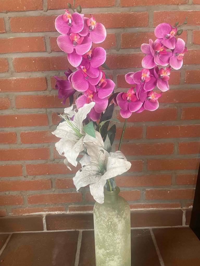 Ein getesteter Kunstblumenstrauss befindet sich in einer weißen Vase vor einer Ziegelwand.