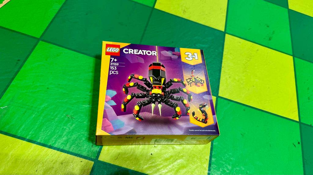 Lego-Creator im Test: Eine Packung mit 153 Einzelteilen einer Spinne in den Deutschlandfarben liegt auf einem grün karierten Bodenbelag.