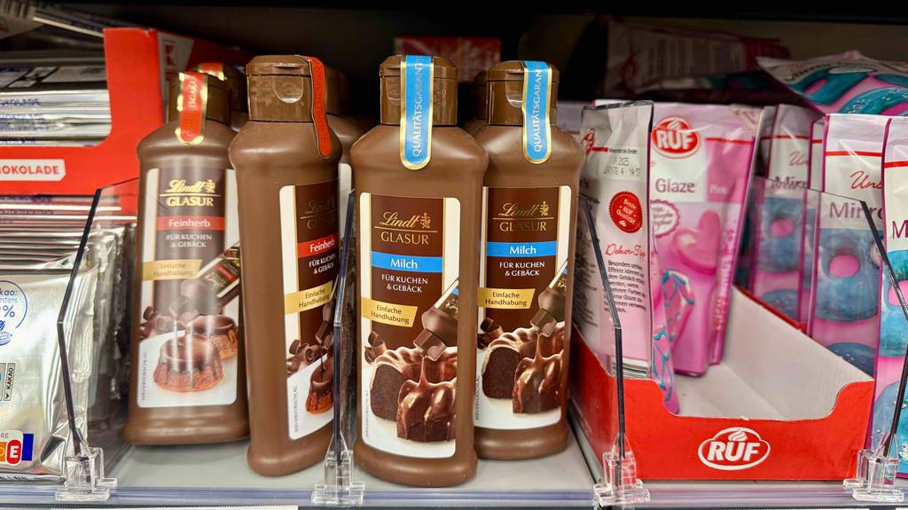 Kuchenglasur im Test: Mehrere braune Quetschflaschen mit Glasur von Lindt in verschiedenen Geschmacksrichtungen stehen neben weiteren Kuchenverzierungen auf einem Verkaufsregal.